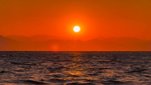 Orange Sun rising over the Sea Horizon with Mountains Silhouette in opposite shore. Beautiful Cinematic Landscape
