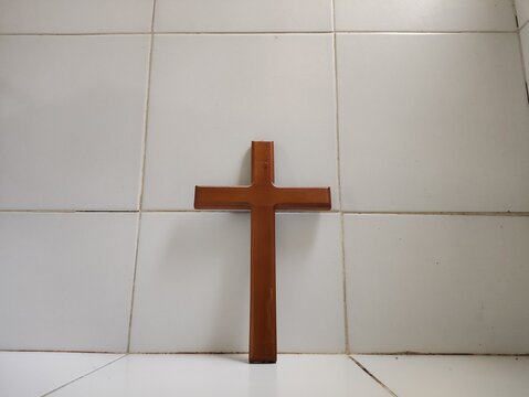 A brown christian cross is centered from a low angle, standing against a tiled background with open copy space.