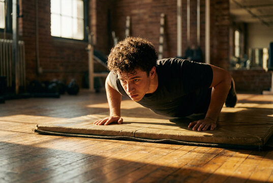 Determined young man performing pushups on a mat in an industrial, sunlit gym