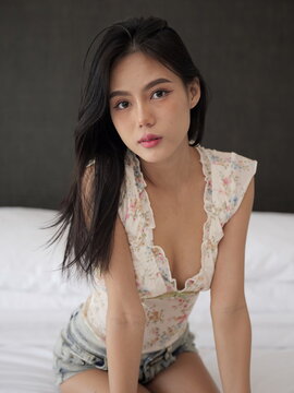 Young Asian woman in a floral crop top and denim shorts kneels on a bed