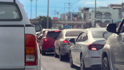 Fototapeta premium Rear view of pickup cars waiting in a heavy traffic jam on an urban highway. Highlighting red tail lights during a busy daytime commute. Many cars were parked in a long queue. In the city of Thailand.