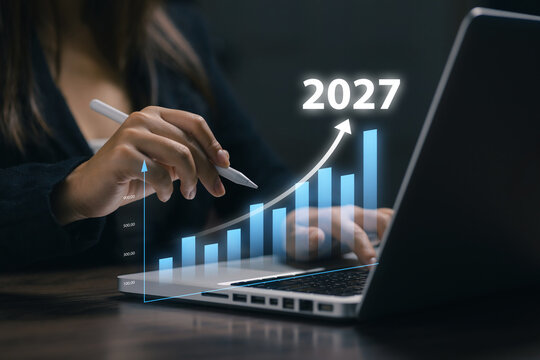 Businesswoman analyzes a rising 2027 bar chart on laptop, representing business growth, financial forecast, investment performance, market strategy, analytics, and economic success.