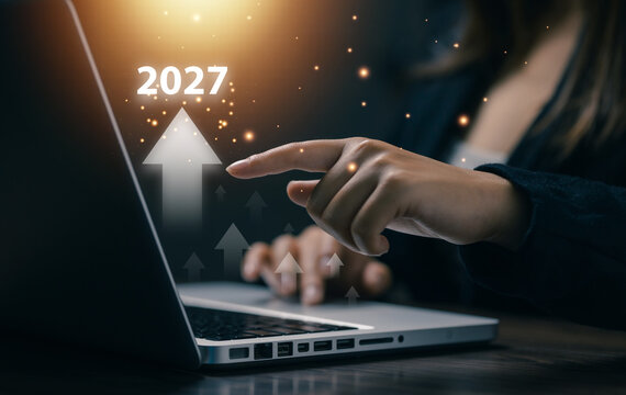 Businesswoman points at laptop with 2027 upward arrows, symbolizing future business growth, economic recovery, financial forecast, strategy, investment, success, and market opportunity.