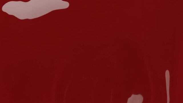Thick glossy crimson paint pools and spreads across a reflective surface, expanding into a smooth puddle under soft overhead lighting against deep black, bold contemporary motion.
