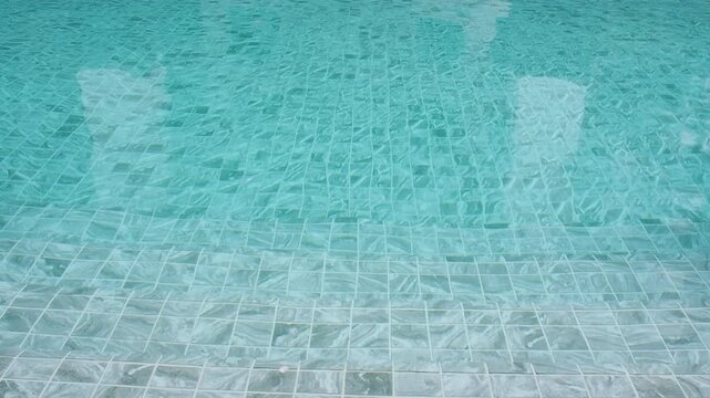 Crystal clear turquoise water in a swimming pool with tiled bottom, showing ripples and reflections