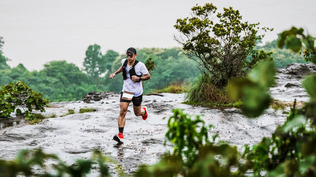 Trail runner racing across a wet rocky mountain trail in the rain surrounded by lush green forest