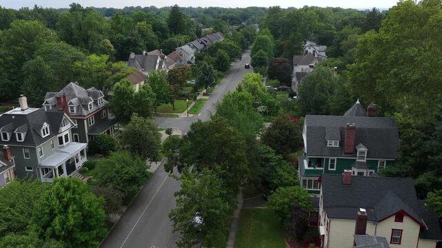 Victorian style houses with turrets line tree shaded street near Seton Hall in South Orange, New Jersey, dense green canopy covers quiet residential neighborhood streets. Aerial drone flyover shot