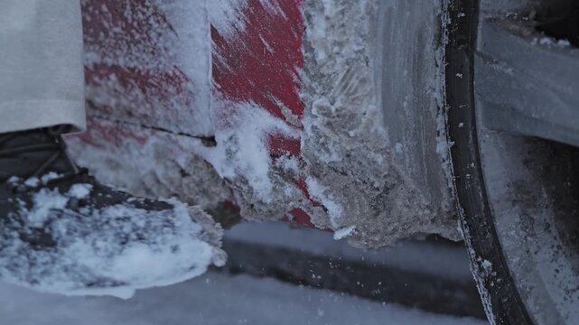 Slow motion winter maintenance showing frozen snow removed from vehicle wheel arch.