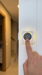 Naklejka premium Close up of a human finger pressing a glowing doorbell button with a bell on a white wall inside a modern residential hallway area
