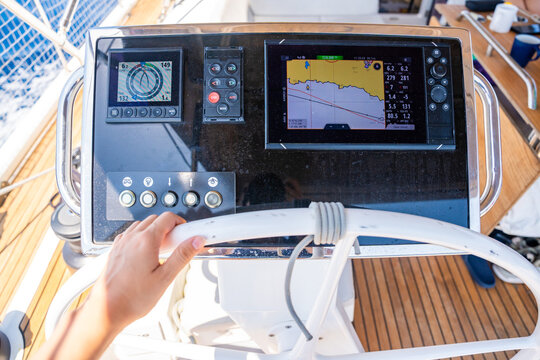 Hand steering a modern sailing yacht using GPS chartplotter and navigation instruments. Marine navigation technology supporting safe offshore sailing and vessel control.