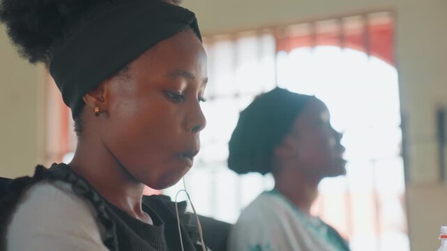Black mother and daughter sitting in sunlit interior, teenage daughter scrolling phone while older mother sits blurred in background quiet domestic moment, intimate bond, warm natural light, candid