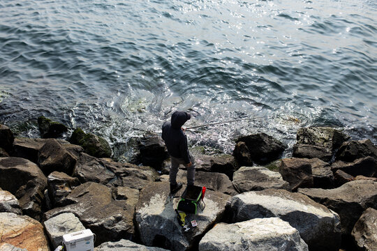 Person fishing on rocky shore near water while using a fishing rod in the daytime