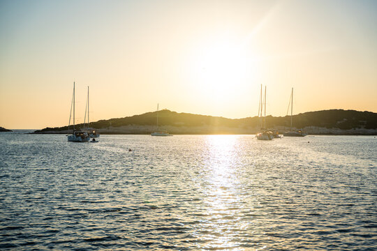 View from bow of sailing yacht anchored in quiet bay during golden sunset with other boats in distance. Concept of slow travel, sailing adventure, anchoring, freedom and peaceful evenings on water