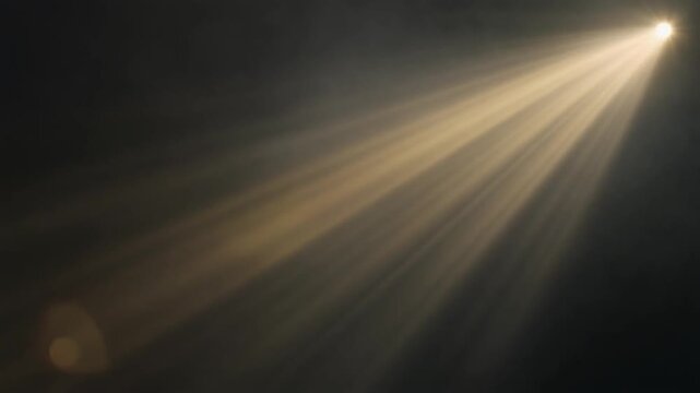 Volumetric golden light rays rotate slowly through atmospheric mist, sweeping diagonally across deep charcoal darkness with cinematic contrast, dramatic haze and generous copy space.