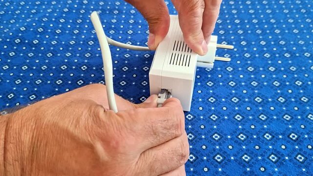 Hands disconnect cable from powerline Ethernet adapter, showing device removal, network setup change, and close up detail of technology used for fast wired internet connection