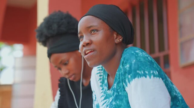 Black mother and child reflecting outdoors, mother gazing toward horizon while daughter writes in notebook with earbuds, soft sunlight, contemplative mood, intergenerational advice and intimate family