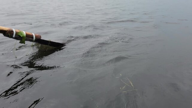 A wooden oar slicing through calm water creating small ripples and spray