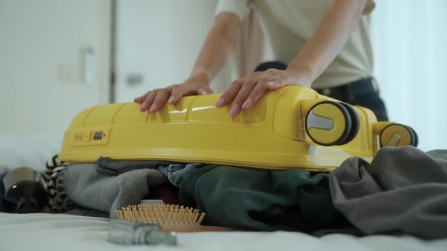 Close-up Stressed young woman struggling to pack an overfilled suitcase before a trip at home. Travel preparation, luggage organization, packing stress. Vacation planning and travel anxiety.
