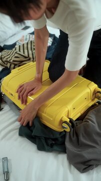 Close-up Stressed young woman struggling to pack an overfilled suitcase before a trip at home. Travel preparation, luggage organization, packing stress. Vacation planning and travel anxiety.
