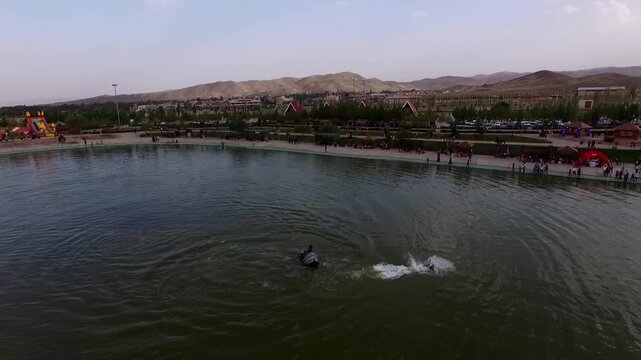 Beautiful aerial panorama of flyboard session on lake with surrounding park area and distant mountains.