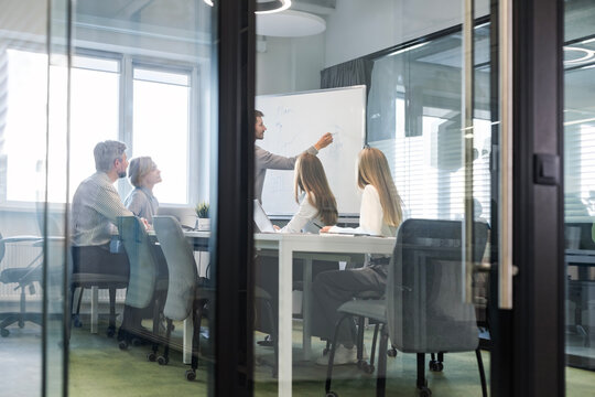A modern office interior, featuring a blurred view of workers at desks, through a glass partition.