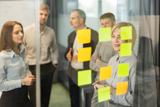 Businesspeople talking in their diverse team during a brainstorming session with sticky notes on glass wall in a modern office