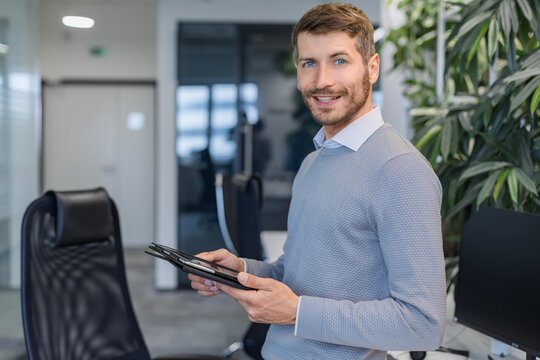 Modern business man in formalwear using digital tablet while standing in the office