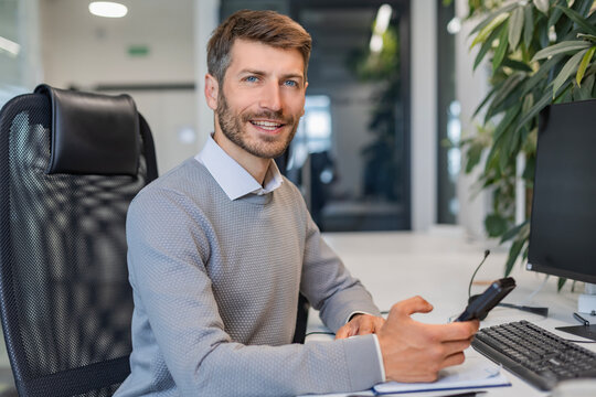 Handsome smiling employee, young entrepreneur looking at camera while sitting in the office