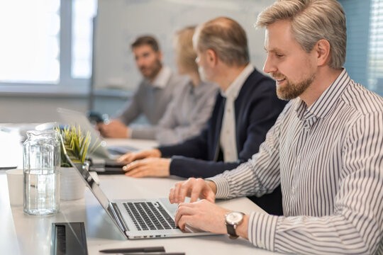 Four business professionals using laptop on desk discussing strategy company