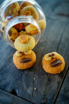 Close-up shot of funny monster face cookies with choco chips topping spilling out from a clear plastic jar onto a dark wooden table. Ideal for concepts of creative baking, kids party snacks, homemade 