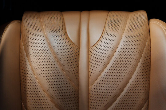 Macro close up of textured perforated brown leather passenger car seat cushion with elegant artistic wave stitching lines in a luxurious premium vehicle cabin. High tech automotive interior design. 