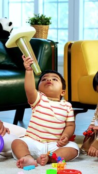 Indian Asian twin infant babies playing with colorful toys while young father and mother sit together on carpet in modern living room at home, capturing joyful family bonding and parenthood moments