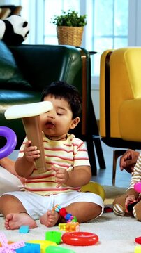 Indian Asian twin infant babies playing with colorful toys while young father and mother sit together on carpet in modern living room at home, capturing joyful family bonding and parenthood moments