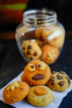 Close-up shot of creative handmade cookies with fun monster face, star, and heart toppings served on white baking paper next to a clear plastic cookie jar. Ideal for concepts of home baking, kids part