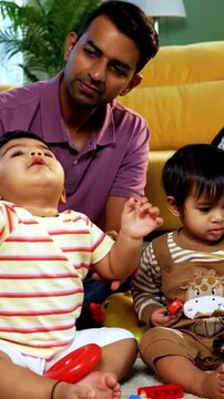 Indian Asian twin infant babies playing with colorful toys while young father and mother sit together on carpet in modern living room at home, capturing joyful family bonding and parenthood moments