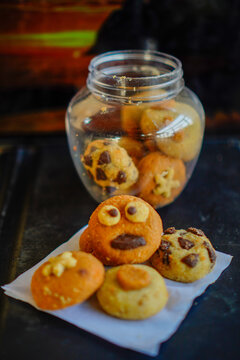 Close-up shot of creative handmade cookies with fun monster face, star, and heart toppings served on white baking paper next to a clear plastic cookie jar. Ideal for concepts of home baking, kids part
