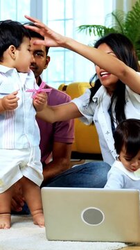 Indian Asian twin infant babies playing with colorful toys while young father and mother sit together on carpet in modern living room at home, capturing joyful family bonding and parenthood moments