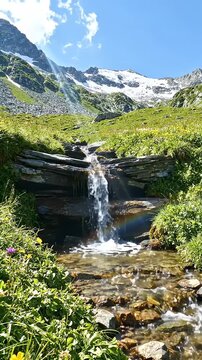Serene Waterfall in Lush Mountain Meadow - A small, cascading waterfall flows over layered rocks in a vibrant green mountain meadow.