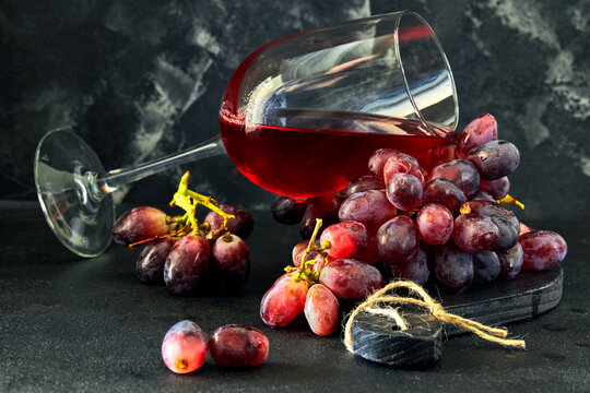Glass of wine with grapes on a black wooden stand and dark background