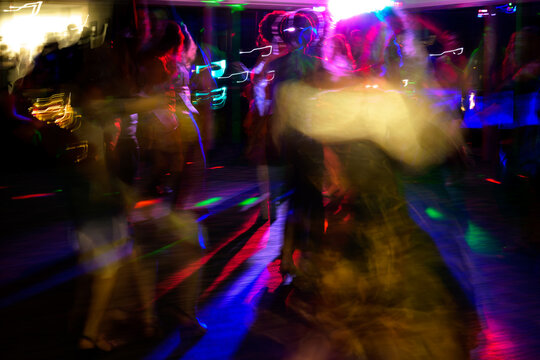 People dancing in a vibrant, colorful atmosphere illuminated by dynamic lights. Featuring motion blur and light trails - horizontal