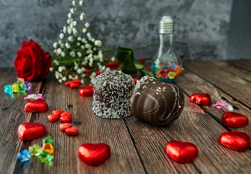 Romantic still life, red rose, chocolate in the shape of hearts and chocolate cakes on wooden background. Valentine's day concept. Soft focus