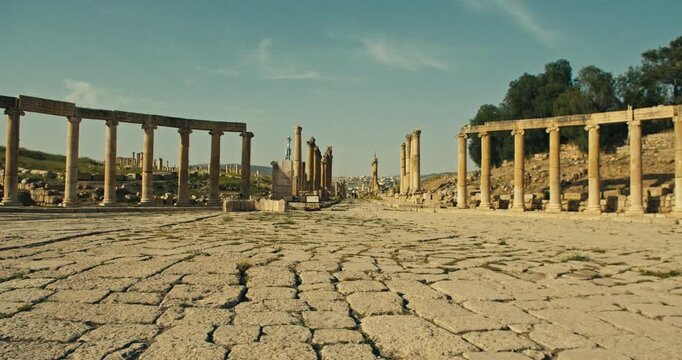 Wide low angle view of the ancient Roman colonnade and stone paved street at the archaeological site of Jerash, Jordan, in warm daylight with a timeless historical atmosphere