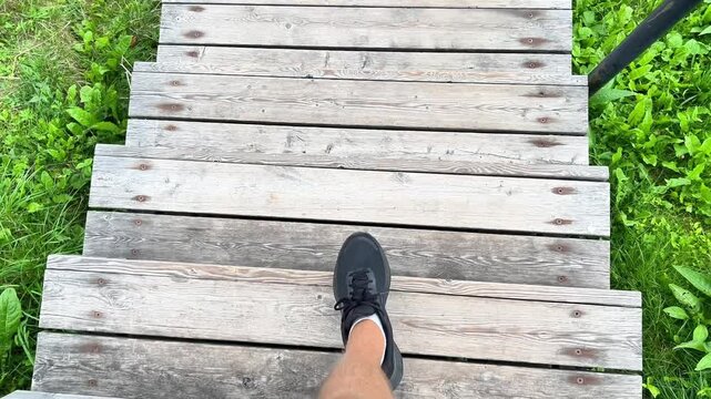 High angle POV shot of a person in sneakers walking down weathered wooden stairs in a park. Ideal for fitness, outdoor activity, lifestyle, travel, and wellness content.