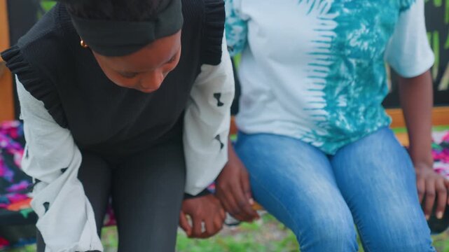 Mother and child sitting on bench in park, candid scene with colorful floral bench cover, casual denim and sweater, child holding smartphone while mother offers quiet support and gentle presence,