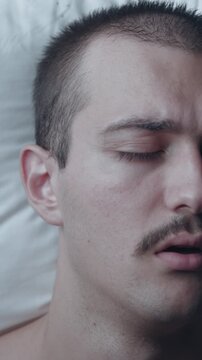 Top-down view portrait of a young Caucasian man with a mustache waking up suddenly in shock and panic from a bad nightmare on a white pillow in bed.