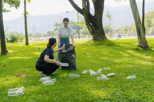 Asian Women Volunteers Collecting Plastic Bottle Garbage into Trash Bag in Green Park for Environmental Protection and Recycling Concept