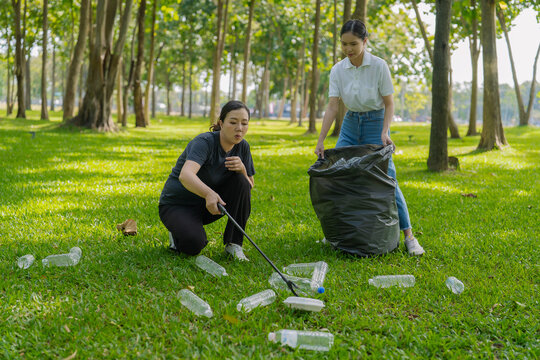 Asian Women Volunteers Collecting Plastic Bottle Garbage into Trash Bag in Green Park for Environmental Protection and Recycling Concept