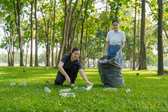 Asian Women Volunteers Collecting Plastic Bottle Garbage into Trash Bag in Green Park for Environmental Protection and Recycling Concept