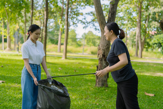Asian Women Volunteers Collecting Plastic Bottle Garbage into Trash Bag in Green Park for Environmental Protection and Recycling Concept
