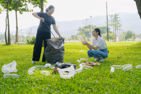 Asian Women Volunteers Collecting Plastic Bottle Garbage into Trash Bag in Green Park for Environmental Protection and Recycling Concept